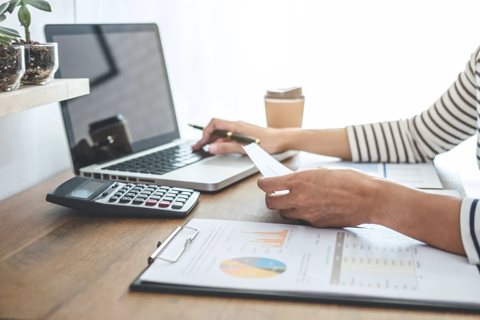 Female entrepreneur working on laptop at desk with paper and calculator