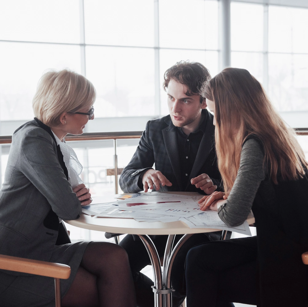 Two young entrepreneurs sitting at table with older, female mentor