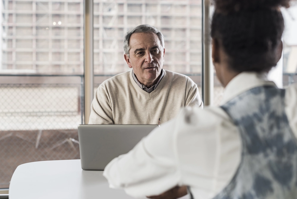 Older business owner at table in discussion with younger successor employee